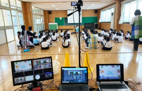 ホールの大型モニタを見る子どもたち