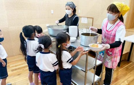 給食を配膳する職員と、器を受け取る園児たち