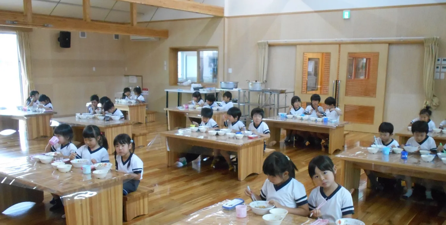 木のランチルームで給食を食べる園児たち